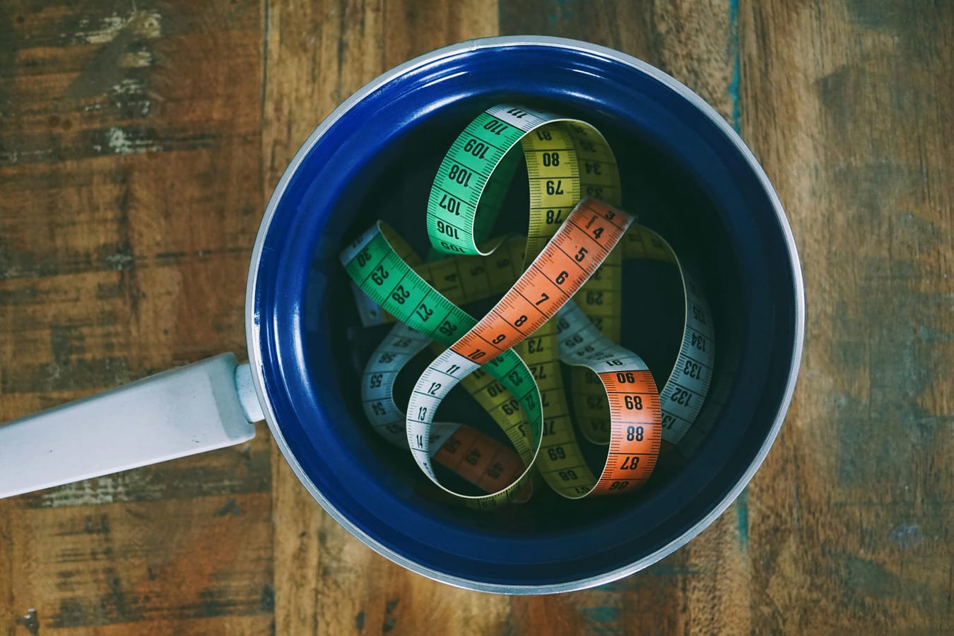 A measuring tape coiled on a wooden surface beside a glass of water in soft natural light.