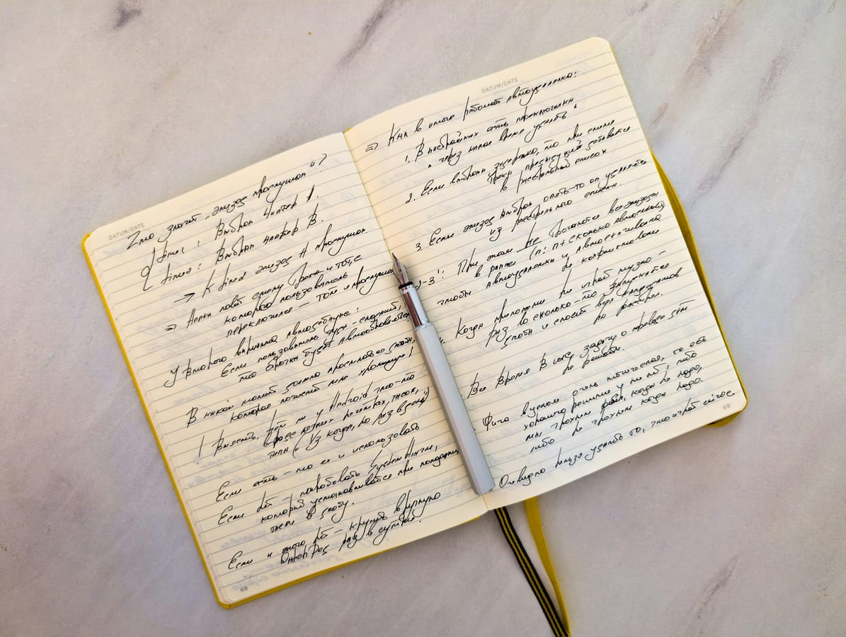 An open notebook with handwritten notes and a pen on a wooden desk in soft natural light.