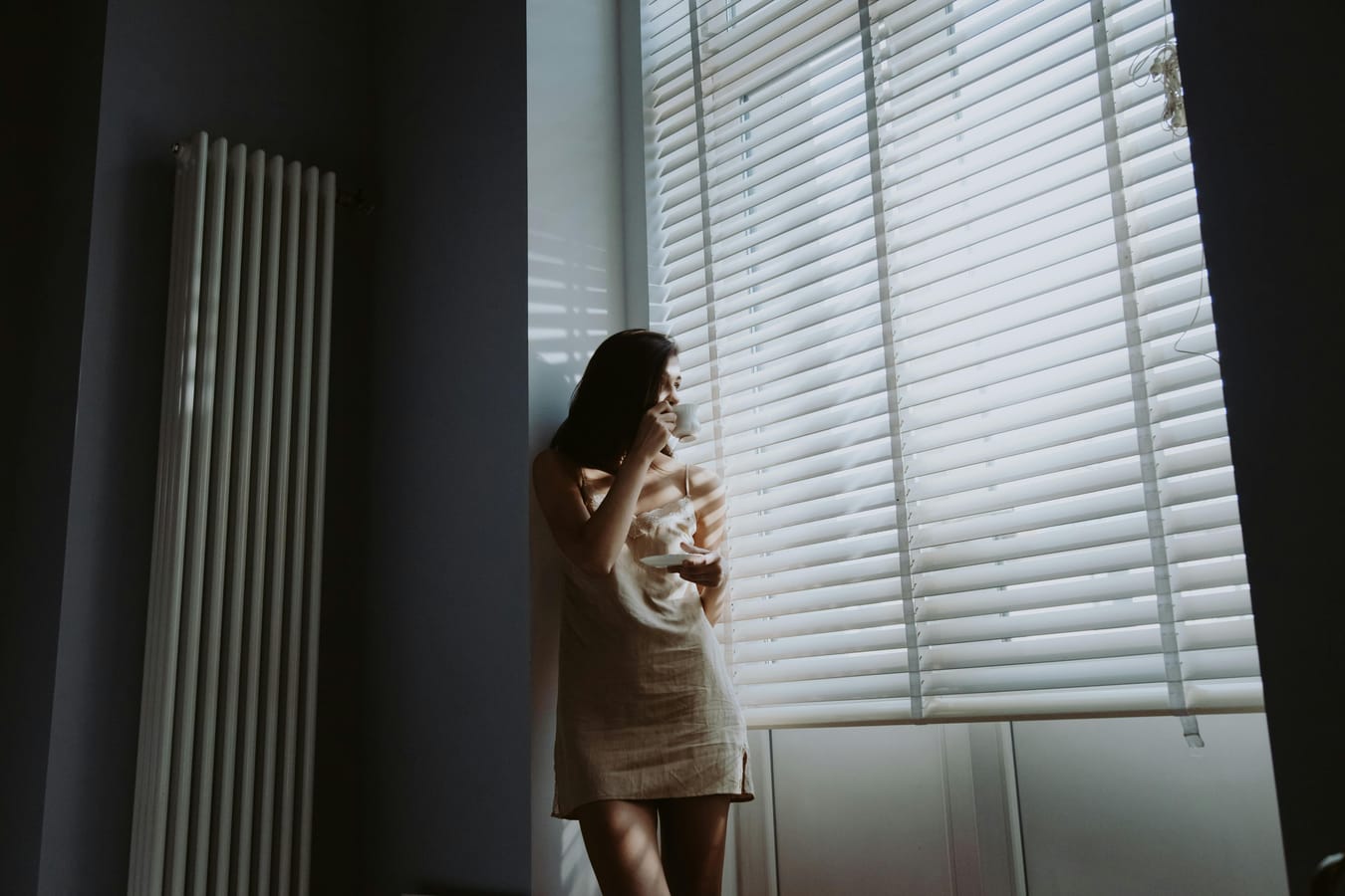 A glass of water and a single white pill on a wooden bedside table, soft morning light.