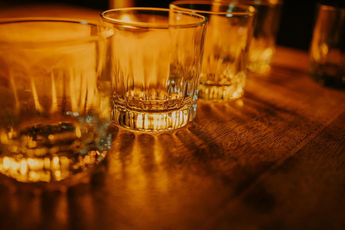 An empty glass on a wooden bar table in soft evening light, suggesting an unhurried drinking session.