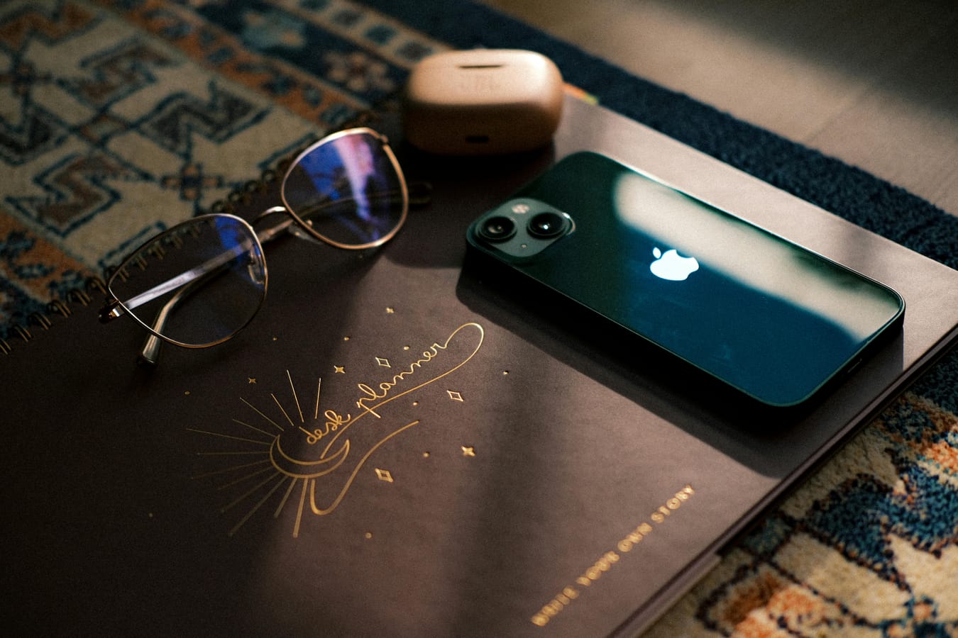 An iPhone on a wooden desk beside a notebook and a glass of water in soft natural light.