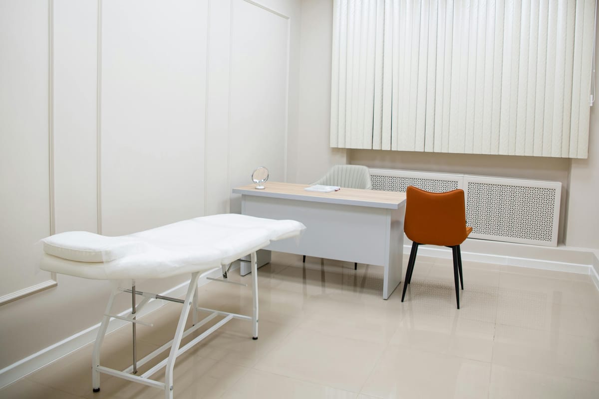 An empty doctor's consultation room with a chair and exam table.