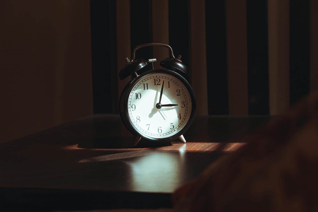 A bedside table with a glass of water and a clock visible in soft early morning light.
