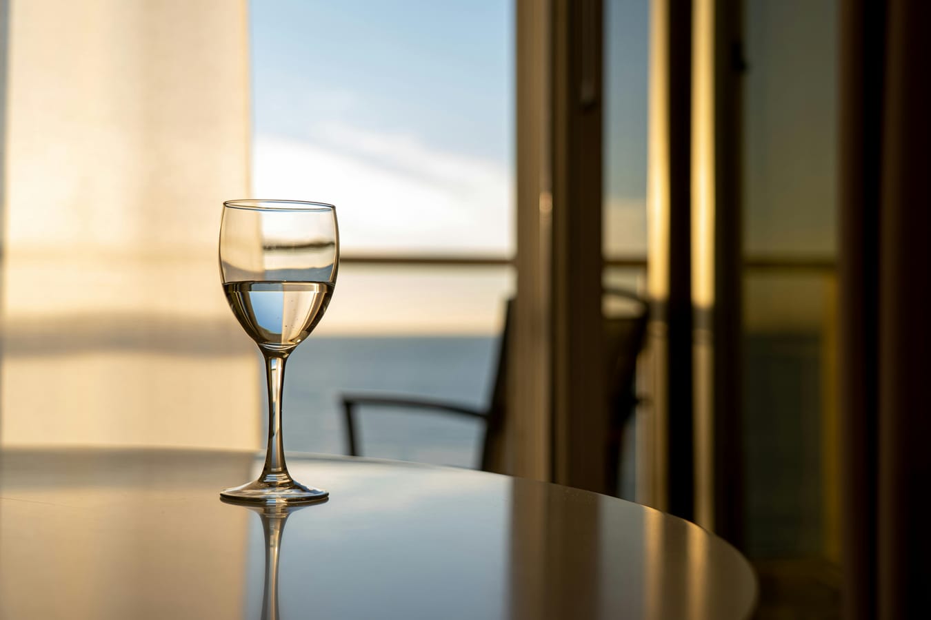 An empty glass of water on a wooden table beside a window with morning light coming through.