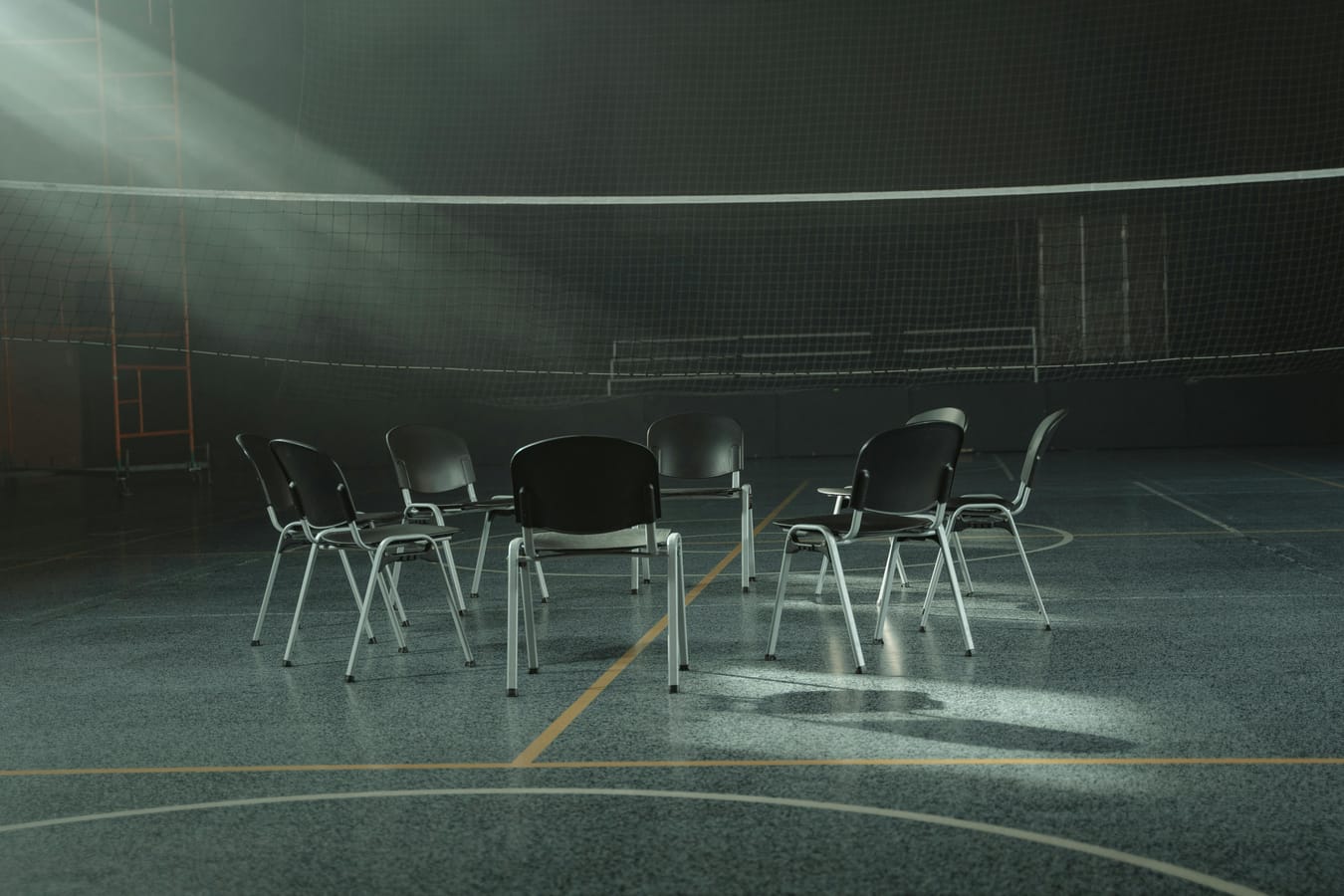 A small group of people sitting in a circle on chairs in a community room with daylight through tall windows.