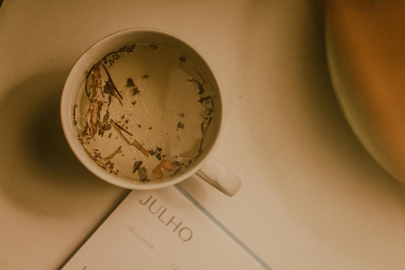 A January calendar with the first few days crossed off, beside a steaming mug of tea on a wooden table.