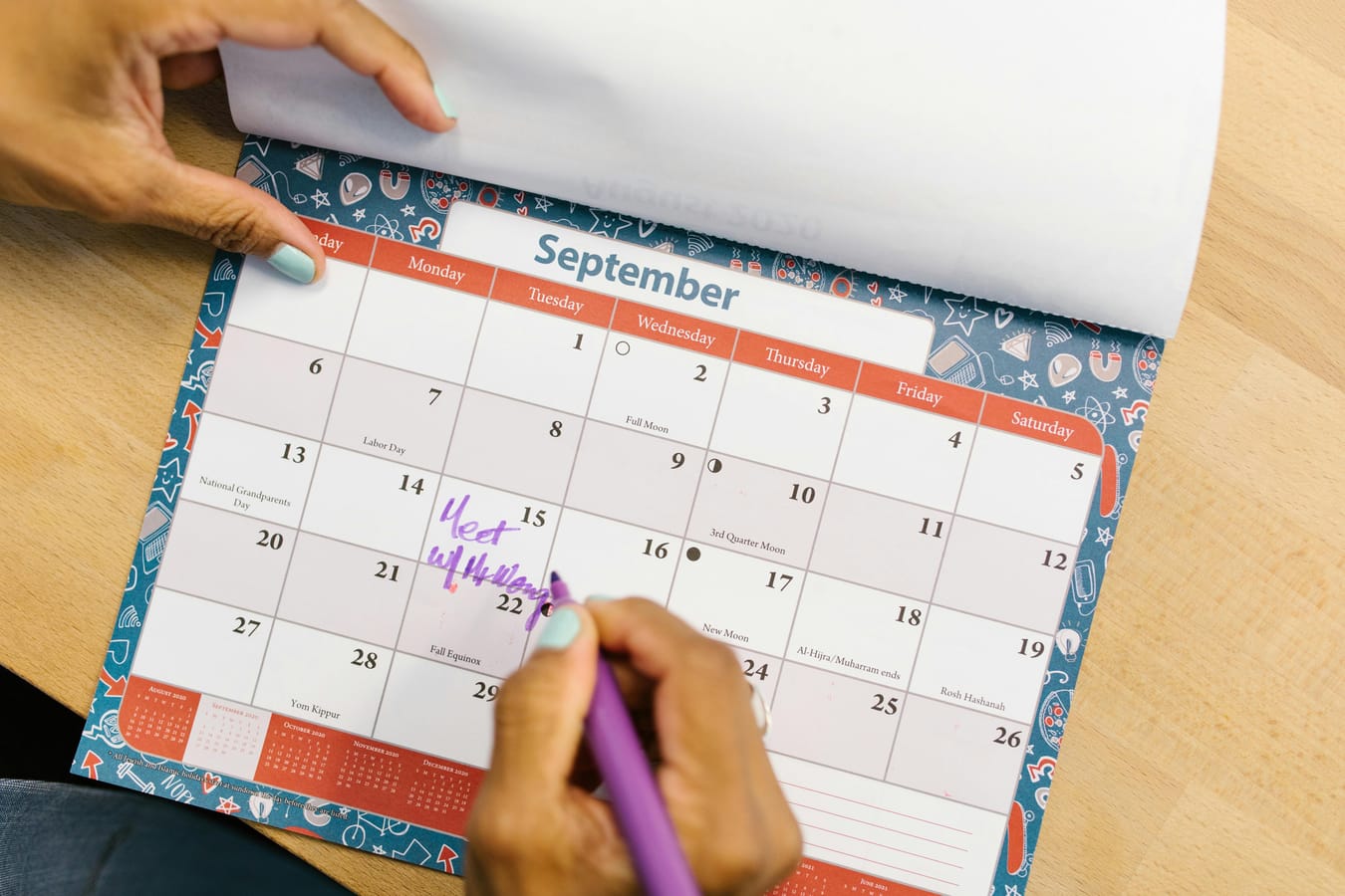 A calendar on a wooden desk with several days marked off, beside a glass of water in soft natural light.